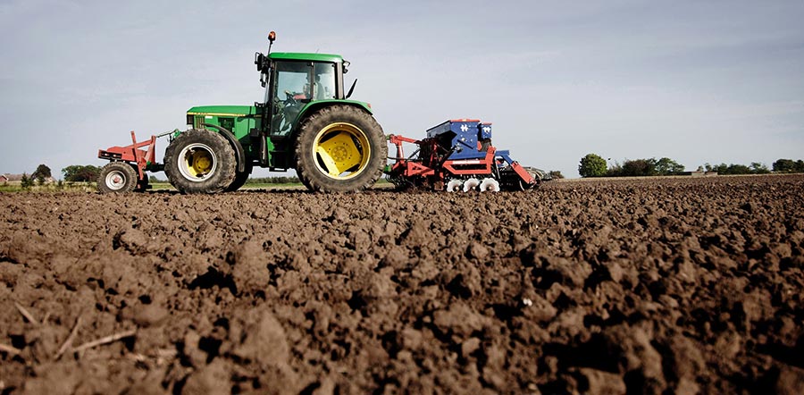 A John Deere tractor pulling a planter over a tilled field